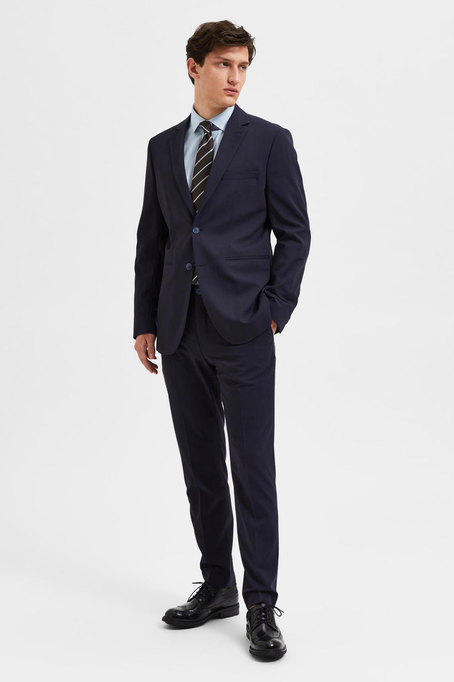 Blazer bleu de SELECTED, porté avec une chemise bleu clair et une cravate rayée.
