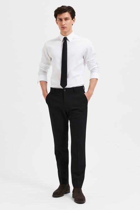Pantalon de costume noir par SELECTED, porté avec une chemise blanche et une cravate noire.