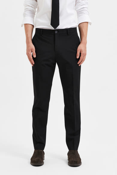 Pantalon de costume noir de SELECTED, porté avec une chemise blanche et une cravate noire, associé à des chaussures marron.
