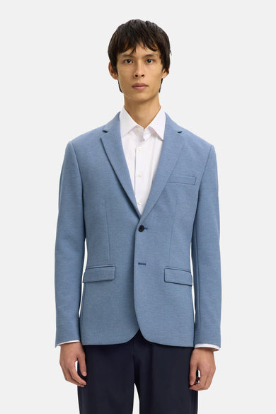 Blauwe blazer van SELECTED, gedragen over een wit overhemd en een marineblauwe broek, met leren schoenen.