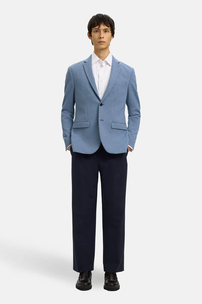 Blauwe SELECTED-blazer, gedragen over een wit overhemd en een marineblauwe broek, met de handen in de zakken.