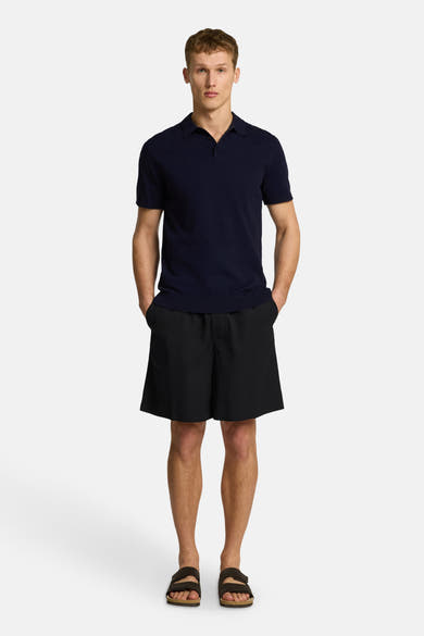 Polo à manches courtes bleu marine de SELECTED, porté avec un short noir et des sandales.
