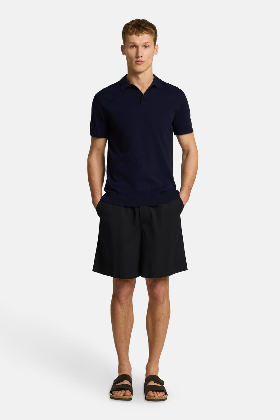 Polo à manches courtes bleu marine de SELECTED, porté avec un short noir et des sandales.
