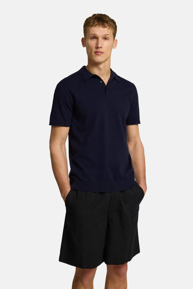 Polo à manches courtes bleu de SELECTED, porté avec un short noir, mains dans les poches.