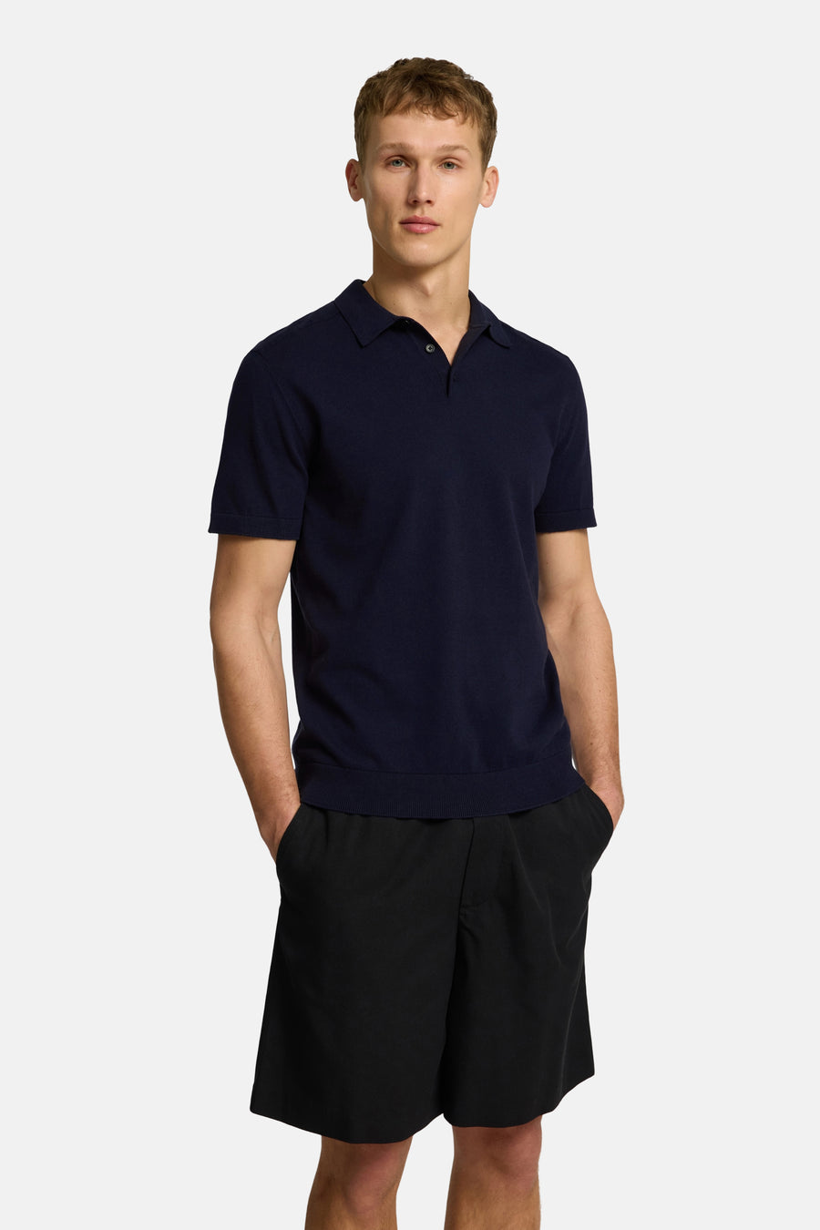Polo à manches courtes bleu de SELECTED, porté avec un short noir, mains dans les poches.