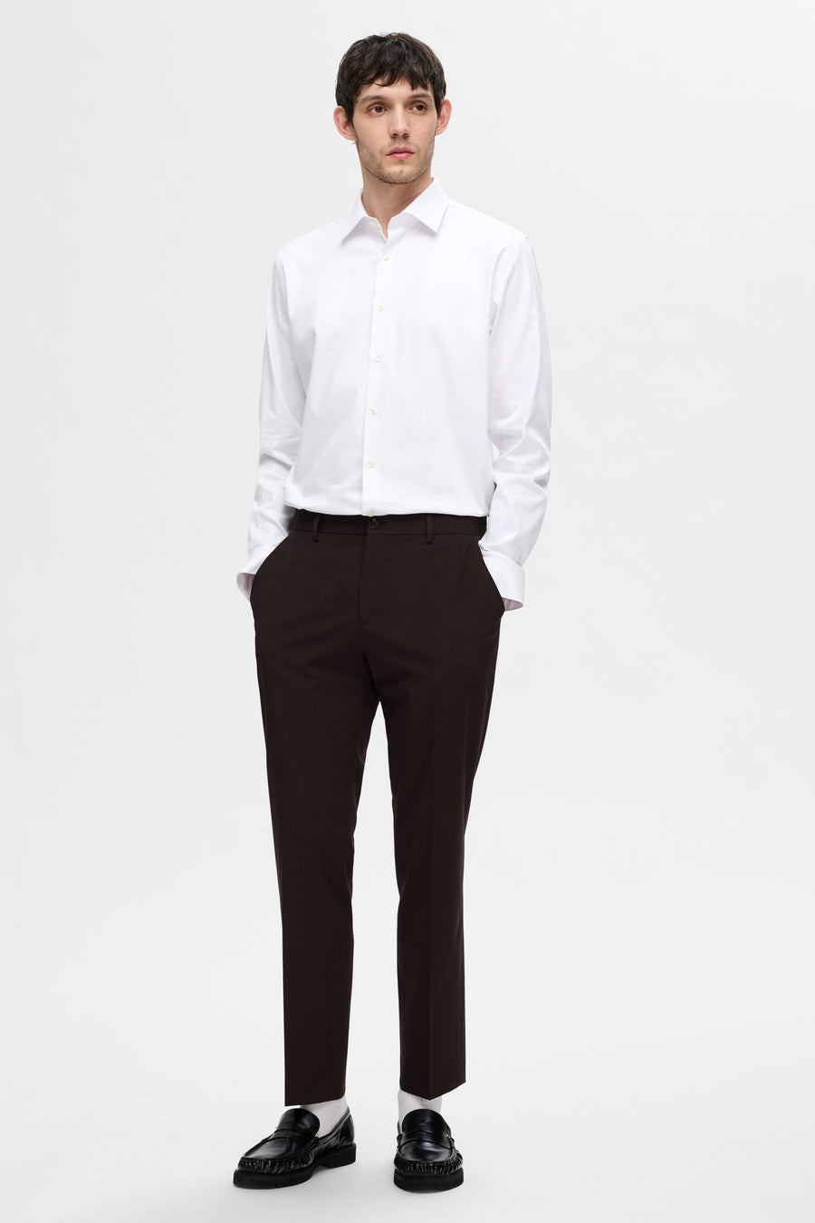 Chemise blanche à manches longues de SELECTED, portée avec un pantalon foncé et des mocassins noirs.