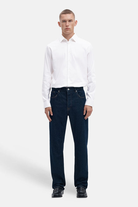 Bright white long-sleeve shirt with classic collar and front buttons, worn with dark denim jeans and black loafers, full-body front view
