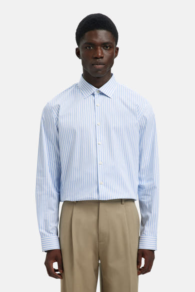 Chemise à manches longues bleue de SELECTED, à rayures verticales, portée avec un pantalon beige plissé.
