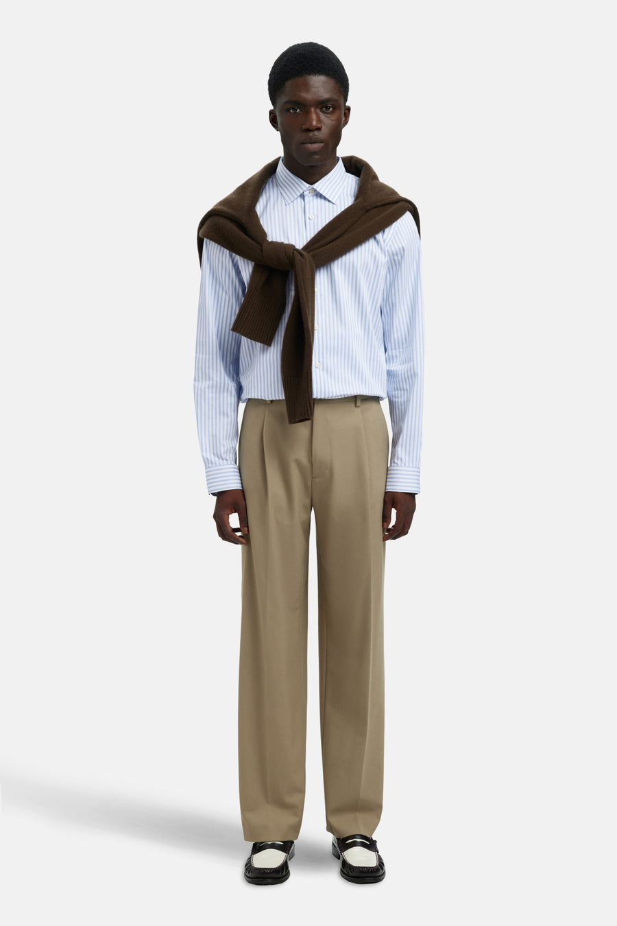 Chemise à manches longues bleue à rayures, de SELECTED, portée avec un pull marron noué sur les épaules et un pantalon beige.