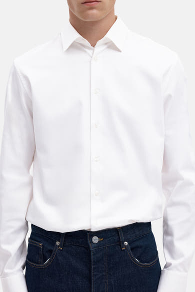 Bright white long-sleeve shirt with classic collar and front buttons, worn with dark denim jeans, cropped front view
