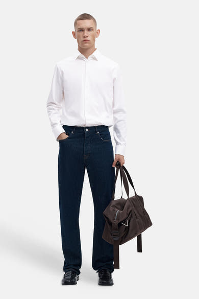 Bright white long-sleeve shirt with classic collar and front buttons, worn with dark denim jeans and black loafers, full-body lifestyle view