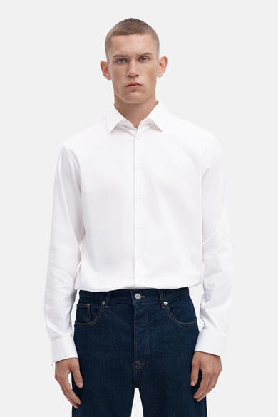 Bright white long-sleeve shirt with classic collar and front buttons, worn with dark denim jeans, front view