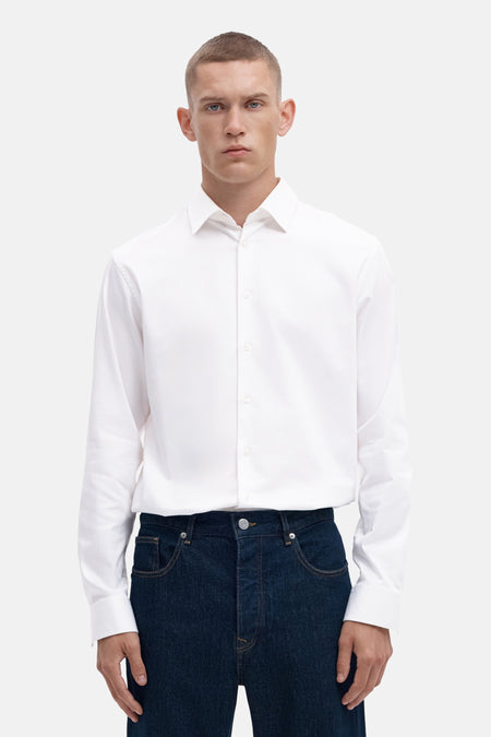 Bright white long-sleeve shirt with classic collar and front buttons, worn with dark denim jeans, front view