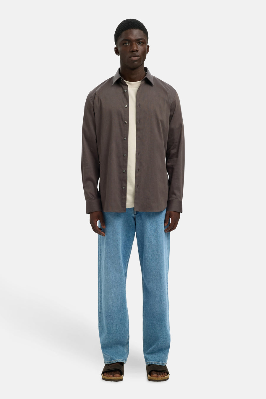 Chemise à manches longues marron de SELECTED, portée ouverte sur un t-shirt clair et un jean bleu décontracté.