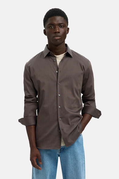 Chemise à manches longues marron de SELECTED, portée sur un t-shirt clair, avec un jean bleu.