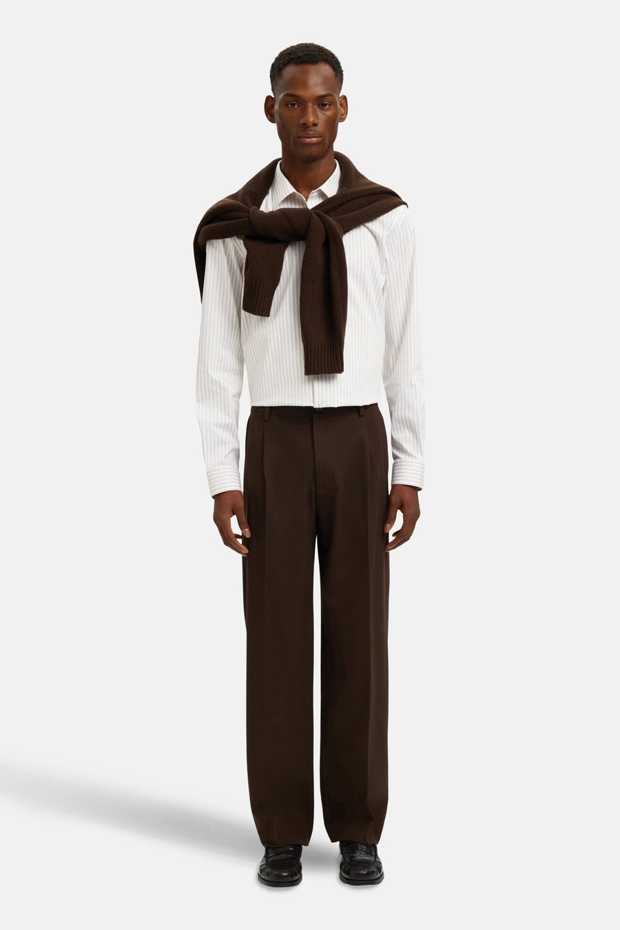 Chemise à manches longues beige rayée de SELECTED, portée avec un pull marron noué sur les épaules et un pantalon marron foncé.