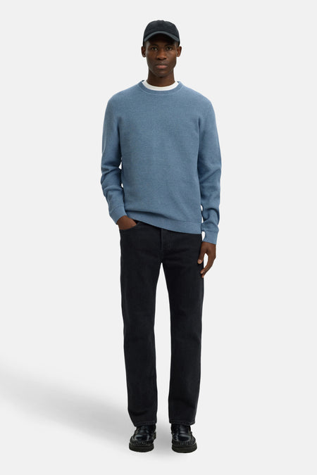 Pull ras du cou bleu de SELECTED, porté avec un jean noir et des mocassins noirs.