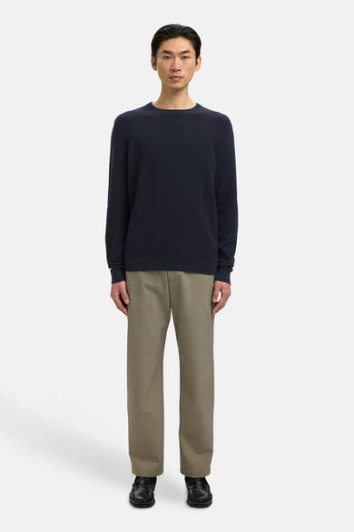 Pull ras du cou bleu foncé de SELECTED, porté avec un pantalon beige et des mocassins noirs.
