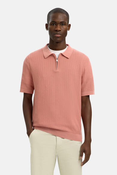 Polo rose en maille par SELECTED, avec fermeture éclair courte et porté avec un pantalon beige.