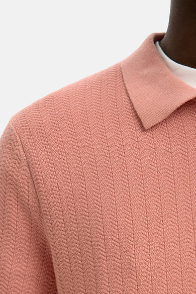 Polo rose SELECTED, à texture en maille et col classique, porté sur un t-shirt blanc.