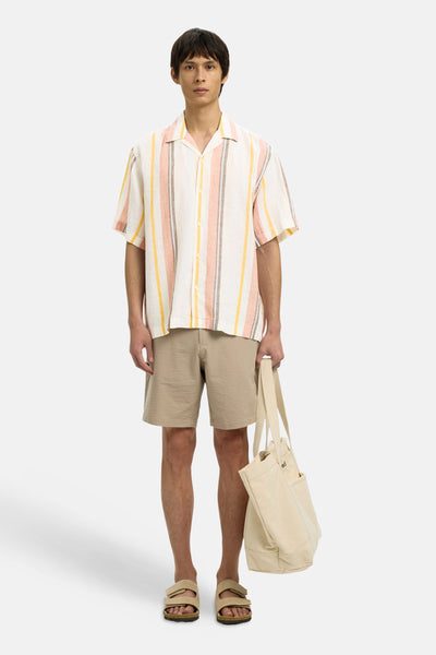 Chemise multicolore à manches courtes de SELECTED à rayures roses, jaunes et grises sur fond clair, portée avec un short, des sandales et un tote bag.