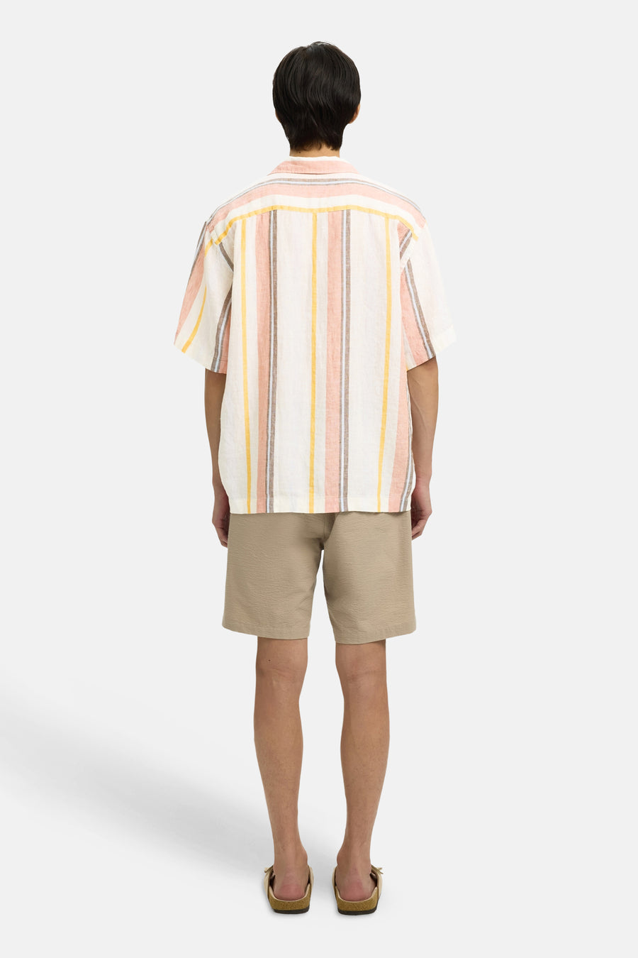 Chemise à manches courtes multicolore de SELECTED, rayée orange, jaune et marron, portée de dos avec un short beige et des sandales.