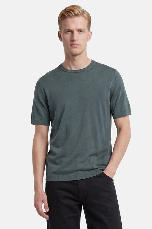 Pull vert en maille fine de SELECTED à col rond et manches courtes, porté avec un pantalon noir.