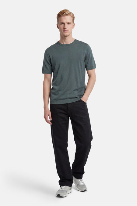 Pull vert en maille de SELECTED à manches courtes et col rond, porté par un homme en jean noir et baskets grises.