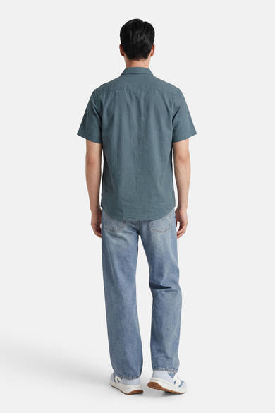 Chemise à manches courtes vert foncé de SELECTED, portée de dos par un homme avec un jean et des baskets.