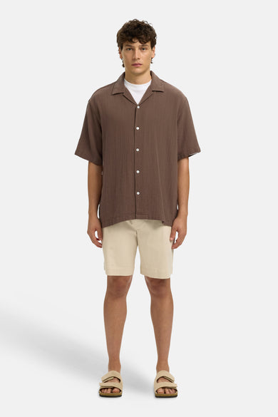 Chemise texturée brune à manches courtes de SELECTED, avec col cubain, portée sur un t-shirt blanc, un short et des sandales beiges.