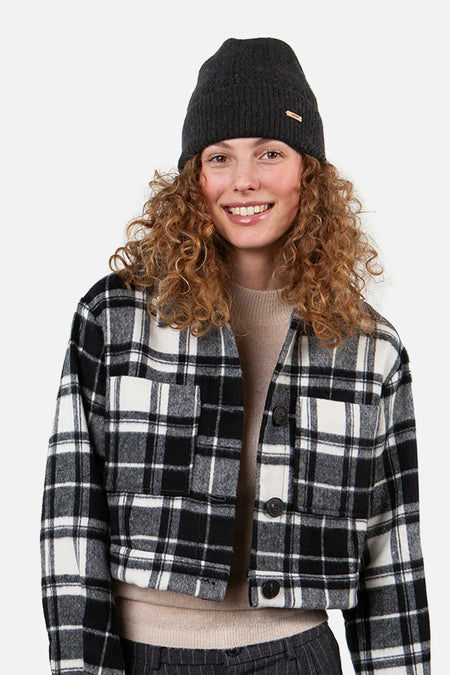 Bonnet noir de Barts, avec petite étiquette logo sur le côté, porté avec une veste à carreaux.