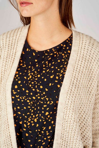 Gilet beige en maille tricotée de Terra di Siena, porté sur une robe noire à motif tacheté orange.