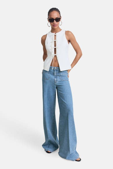 Jeans larges en denim bleu moyen de MANGO, avec des poches sur le devant, portés avec un top blanc.
