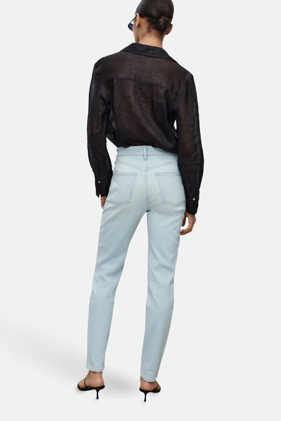 Jean Mom bleu clair de MANGO, porté avec une chemise noire transparente et des chaussures à talons.