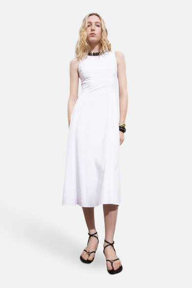 Witte MANGO jurk, midi-lengte en uitlopende pasvorm, gedragen met een ketting en zwarte sandalen.