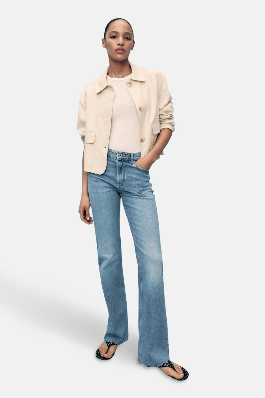 Lichtblauwe uitlopende jeans van MANGO, gedragen met een beige jasje en gestippelde sandalen.