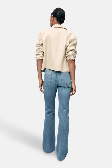 Lichtblauwe uitlopende jeans van MANGO, achterkant, gedragen met een beige jas.