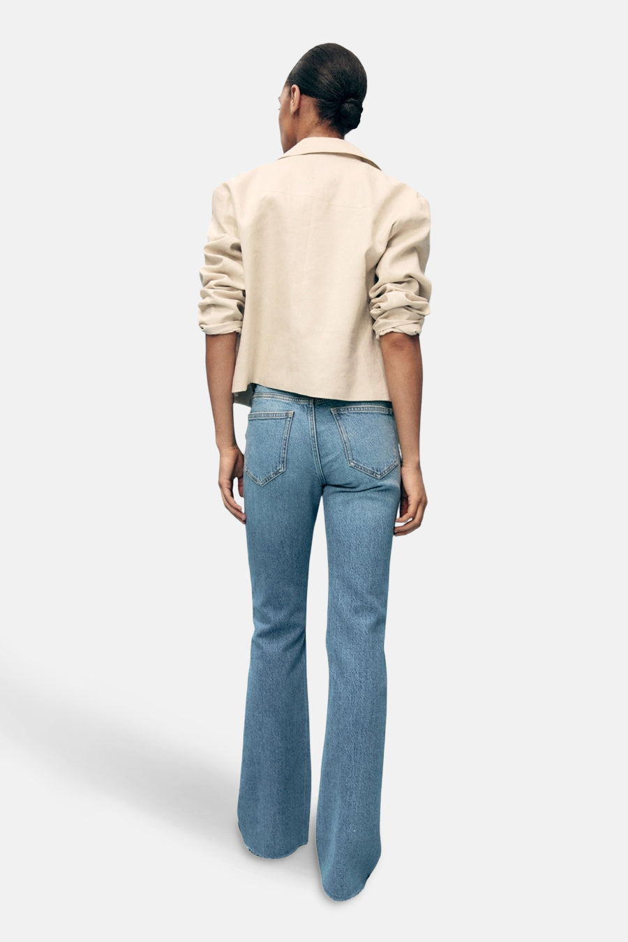 Lichtblauwe uitlopende jeans van MANGO, achterkant, gedragen met een beige jas.