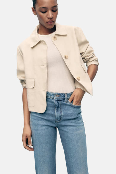 Lichtblauwe flared jeans van MANGO, gedragen met een beige jasje en een crèmekleurig T-shirt.