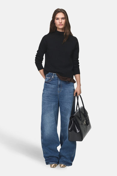 Pull à col rond noir de MANGO, porté avec un jean ample bleu et un sac à main noir.