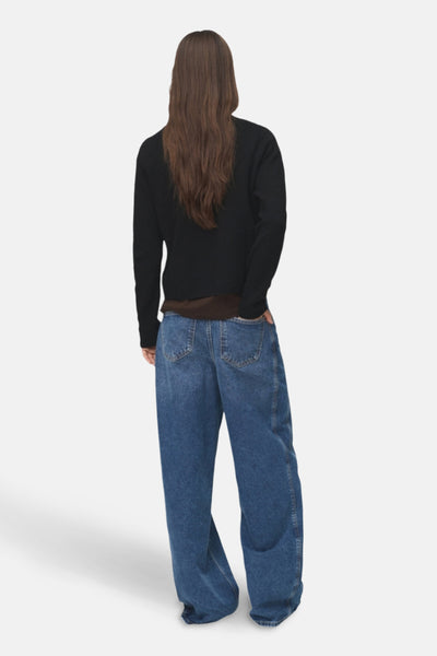 Pull à col rond noir de MANGO, porté avec un jean ample bleu et un t-shirt marron, vue de dos.