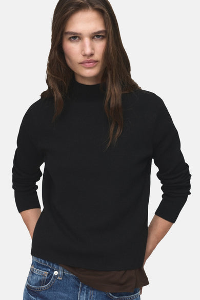 Pull à col rond noir de MANGO, porté avec un jean bleu décontracté.