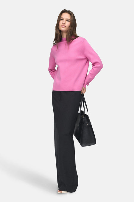 Pull ras du cou rose par MANGO, porté avec un pantalon noir ample et un sac noir.