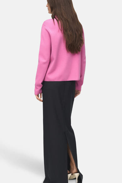 Roze rondehals trui van MANGO, gedragen met een lange zwarte rok met split aan de achterkant.