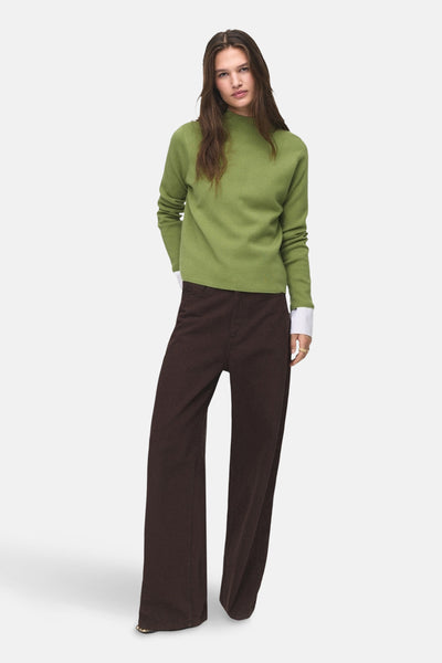 Pull à col rond vert de MANGO, avec manches longues, porté avec un pantalon marron ample.