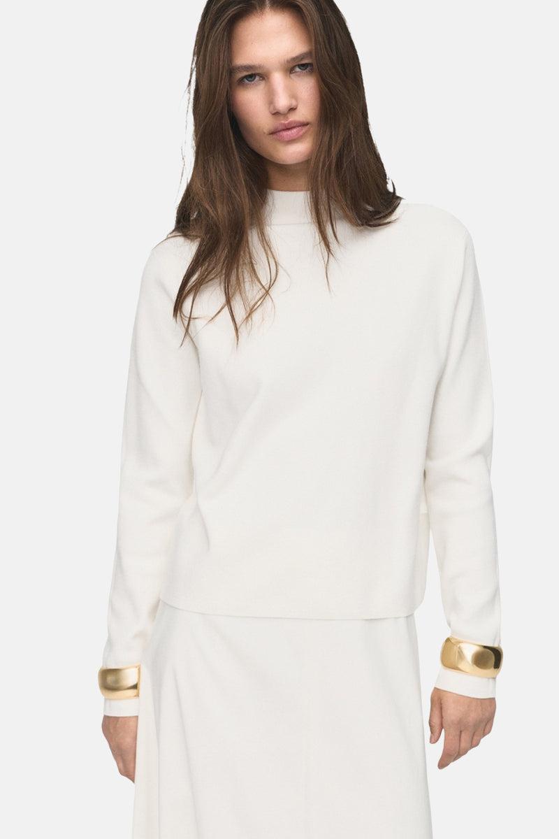 Witte rondehals trui van MANGO, gedragen met een lange witte ballonrok en gouden armbanden.