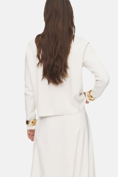 Witte rondehals trui van MANGO, gedragen met een bijpassende witte rok en gouden armbanden, achtergezicht.