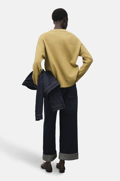 Pull à col rond vert par MANGO, porté avec un jean brut à revers et une veste en denim.