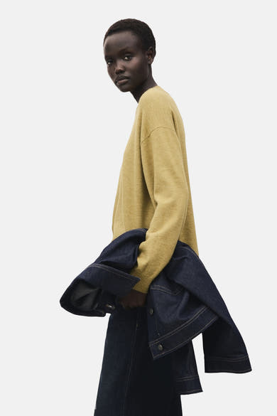 Pull à col rond vert de MANGO, porté avec une veste en jean bleu foncé et une jupe assortie.