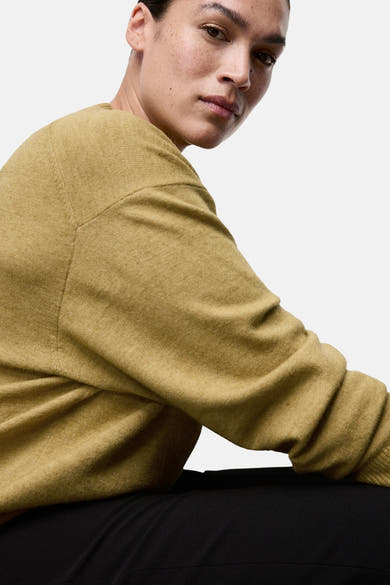 Pull à col rond vert de MANGO, en maille fine, porté avec un pantalon noir, en gros plan.
